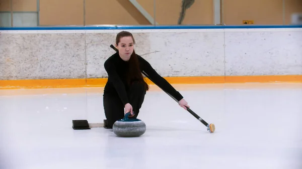 Curling training - een jonge vrouw met lang haar duwt van de tribune met een stenen bijter — Stockfoto