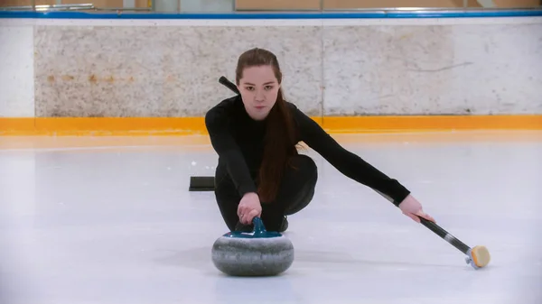 Curling treinamento - uma jovem mulher com cabelos longos na pista de gelo segurando uma pedra de granito — Fotografia de Stock