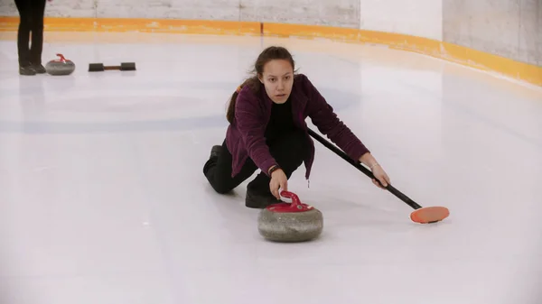 Curling - en kvinna knuffar iväg på isfältet med en granitsten — Stockfoto