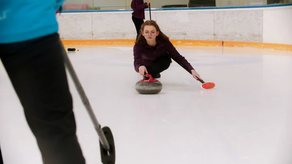 Curling - una donna spinge fuori nel campo di ghiaccio con una pietra di granito — Foto Stock