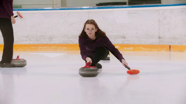 Curling - una giovane donna in occhiali spinge fuori nel campo di ghiaccio con una pietra di granito — Foto Stock