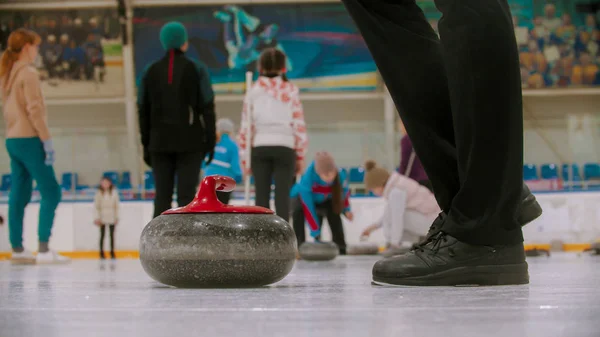 Curling training - una piedra de granito con mango rojo y una persona de pie cerca —  Fotos de Stock