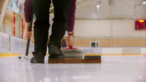 Allenamento di curling al chiuso - una donna che sta per spingere giù dal banco sul campo di ghiaccio — Foto Stock