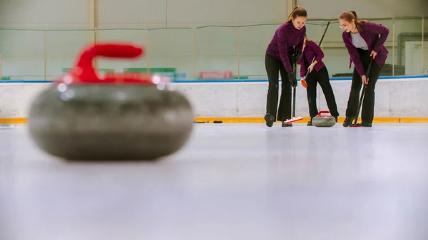 Trening curlingu - prowadzący granitowy kamień na lodzie - dwie kobiety pocierające lód przed kamieniem — Zdjęcie stockowe