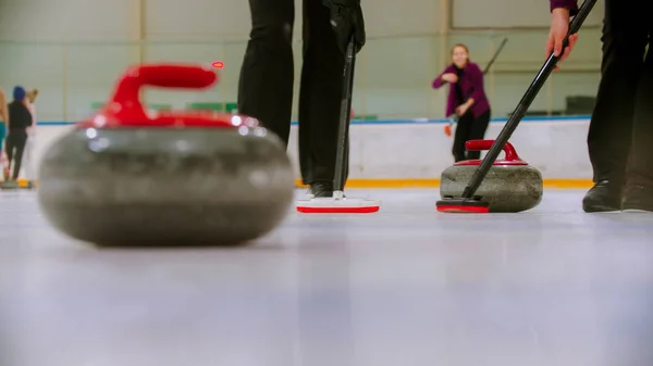 Curling entrenamiento en la pista de hielo un mordedor de piedra de granito con mango rojo golpear a otro mordedor del equipo opuesto —  Fotos de Stock