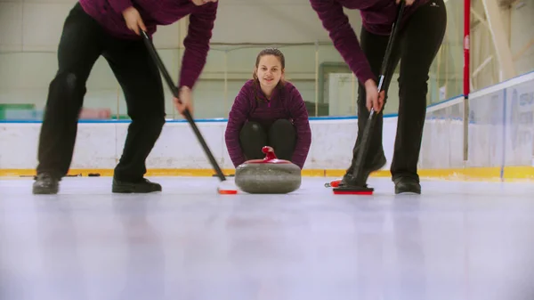 Curling - guiando la piedra de granito en el hielo y frotando el hielo antes de la piedra - una mujer observando el proceso — Foto de Stock