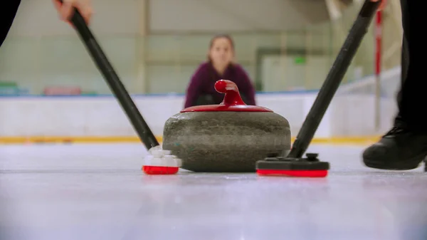 Trening curlingu na lodowisku - prowadzenie granitowego kamienia na lodzie i pocieranie lodem przed kamieniem - kobieta obserwująca proces — Zdjęcie stockowe