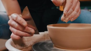 Kürek kemiğini kullanarak çömlekçilik yapan adam, kenarlardaki fazlalıkları temizler.