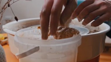 Adam çömlekçi, kilden tencere yontuyor, ellerini suya sokuyor.