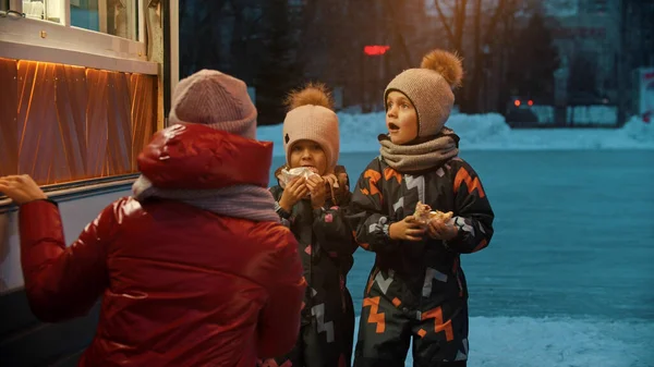 Junge Frau gibt ihren Kindern Heißgetränke in der Nähe eines kleinen Ladens - Winterzeit — Stockfoto