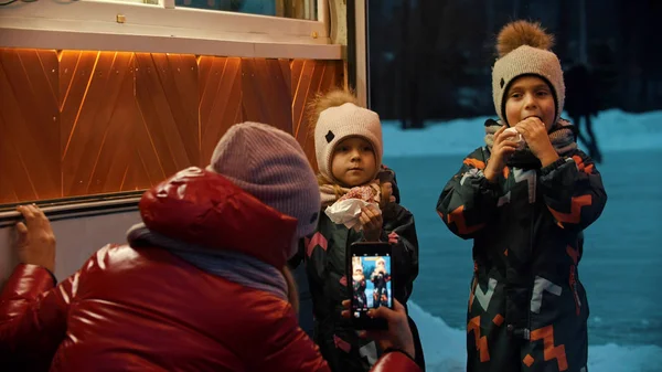 Een jonge vrouw die foto 's maakt van haar kinderen die warme dranken drinken en buiten donuts eten in de winter — Stockfoto