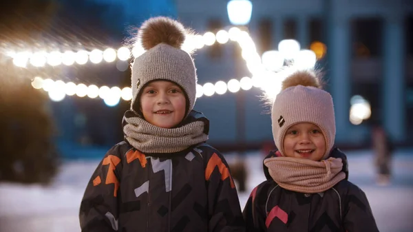 Twee kleine kinderen staan op de openbare ijsbaan en zwaaien met hun handen - kijkend in de camera — Stockfoto