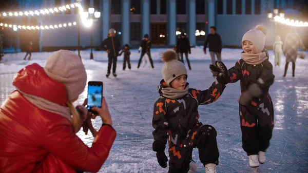 Zwei kleine Kinder auf der Eisbahn - ihre Mutter filmt sie mit der Handykamera - Kinder posieren — Stockfoto