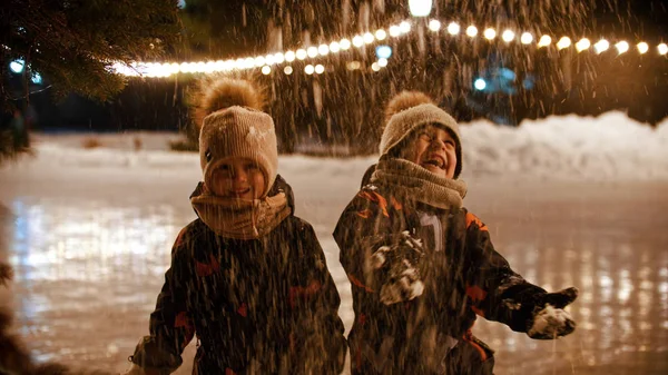 Twee kleine kinderen die op de ijsbaan staan en sneeuw in de lucht gooien — Stockfoto