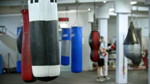Egy bokszzsák lóg a tornateremben - férfi bokszoló sétál a háttérben — Stock videók
