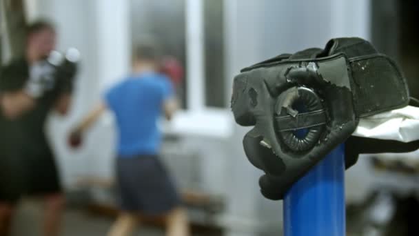 Beschädigter Schutzhelm in der Turnhalle - zwei Männer im Hintergrund bei einem Trainingskampf — Stockvideo