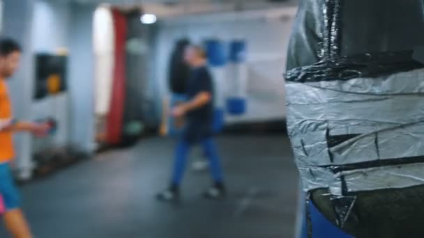 Un gimnasio para el entrenamiento de artes marciales - saco de boxeo colgante - entrenamiento de los hombres en el fondo — Vídeo de stock