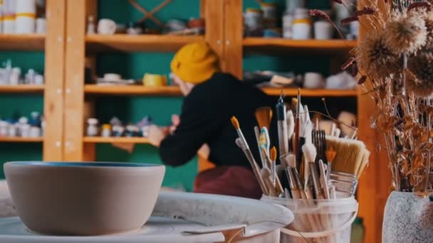 Taller de cerámica - diferentes instrumentos para hacer platos de barro - un hombre camina hacia los estantes y toma una pintura de ella — Vídeo de stock