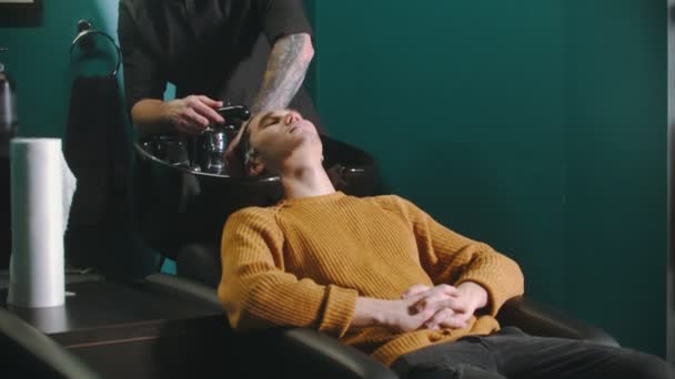 Mężczyzna fryzjer z tatuażami myje włosy klienta — Wideo stockowe