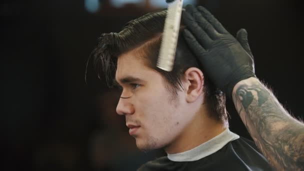 Um jovem cortando o cabelo na barbearia perto do barbeiro tatuado — Vídeo de Stock