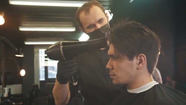 Un joven guapo recibiendo un servicio del peluquero tatuado secando el cabello después del corte de pelo — Vídeos de Stock