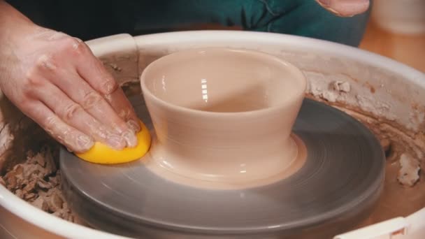 Aardewerk - de meester veegt het pottenbakkerswiel af met een gele spons — Stockvideo