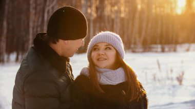 A married couple looking at each other outdoors at winter near the forest