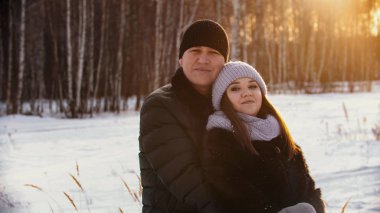A married smiling couple hugging outdoors at winter near the forest