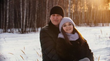 A married couple hugging outdoors at winter near the forest