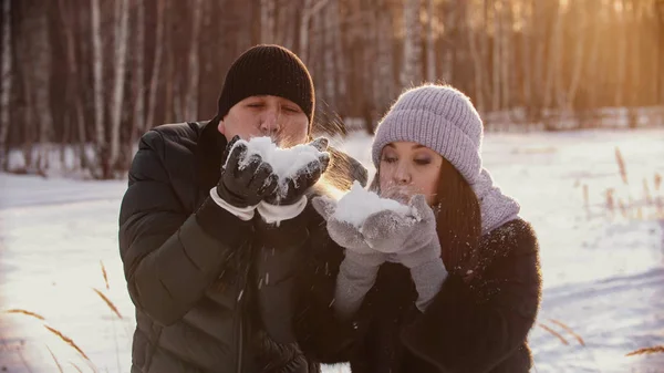 A married cute couple blowing out snow from their hands — 스톡 사진
