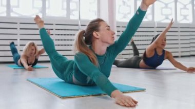 Yoga minderinde yatan, karnının üstüne uzanan ve egzersiz yapan genç kadınlar.