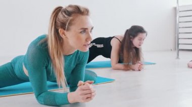 Yoga minderinde antrenman yapan genç kadınlar. Karnının üstüne yatıp esneme hareketleri yapıyorlar.