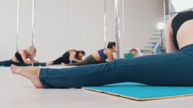 Yoga minderinde oturup bacaklarını esneten genç kadınlar.