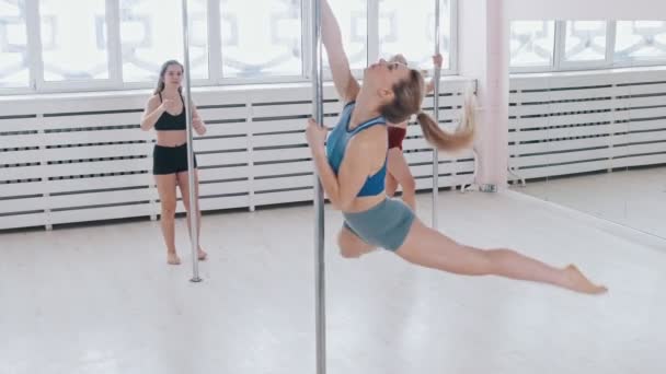 Młode kobiety trenują taniec na rurze w jasnym studio - skacząc na rurze i wirując na niej — Wideo stockowe