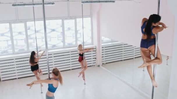 Young women spinning on the poles in bright white studio — Stock video