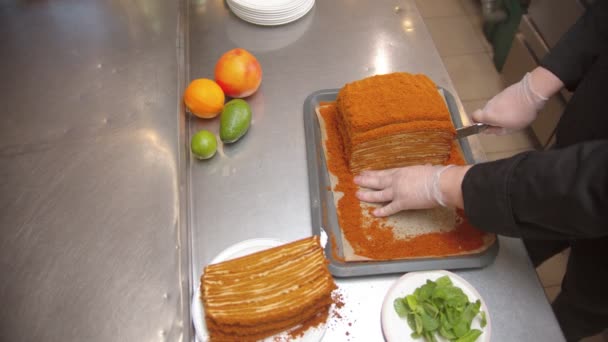 Chef cutting a big piece out of honey cake using a sharp knife - fruits lying near on the table — Αρχείο Βίντεο