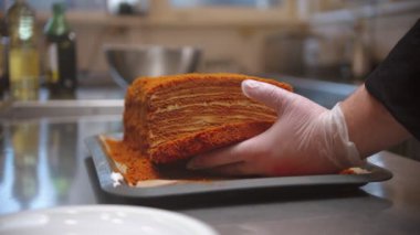 Chef cutting a big piece out of honey cake and put in on the separate plate