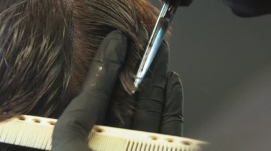 Berber müşterileri ince bir makasla şakaklarına ıslak saç kesiyor.