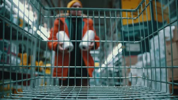 Cesta de supermercado - um homem em uma jaqueta laranja está colocando produtos domésticos em um carrinho — Vídeo de Stock