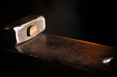 Karanlıkta örsün üzerinde parlayan bir çekiç.