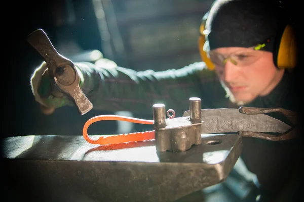 A man blacksmith in protective glasses making a unique handle for the knife - bending the metal — Stock Photo, Image