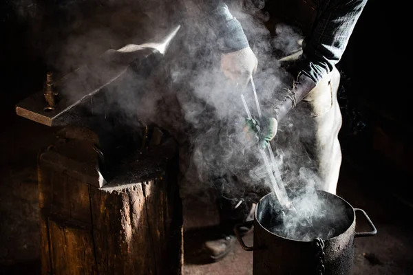 Smid man zet een brandend item in de emmer water - stoom komt uit — Stockfoto