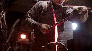 Demirci bir adam, bükülmüş bir metal parçasını eğiyor.