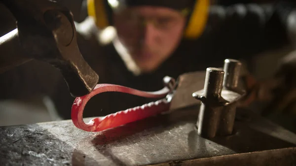 Blacksmith forging a metal handle with unusual design using a hammer