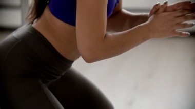 Young woman trainer squatting while fitness training indoors