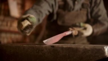 Demirci, kasvetli bir atölyede bıçak dövüyor.