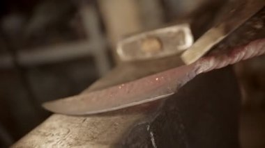 Blacksmith brushing the knife blade - sparkles and fire comes off the blade