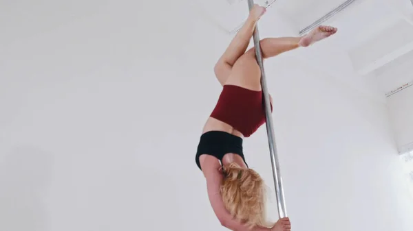 Una donna bionda in abiti sportivi con un allenamento di pole dance in studio - mantenendo l'equilibrio capovolto — Foto Stock