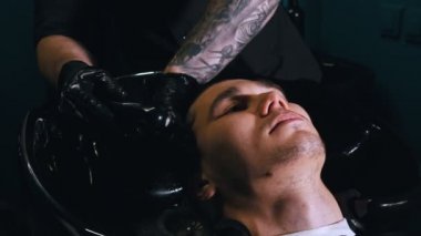 Siyah maskeli bir adam müşterisinin saçını siyah lavaboda yıkıyor.