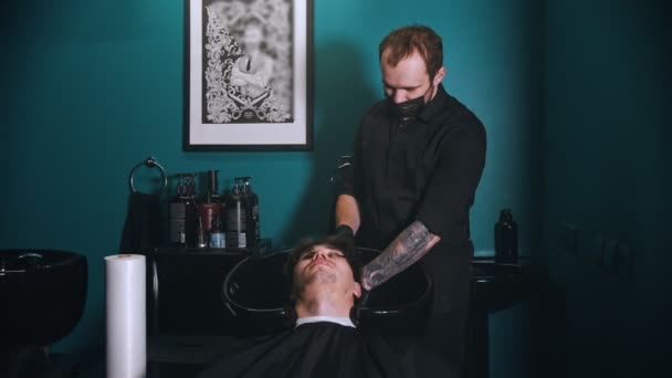 Barbería humana en máscara negra lavando el cabello de su cliente en barbertería. — Vídeos de Stock